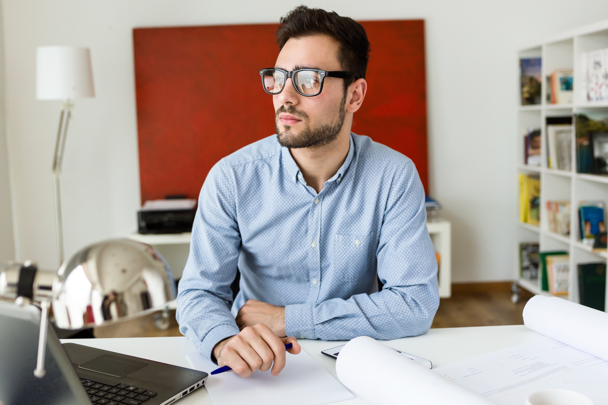 Man sat at desk with paper in front of him, thinking.